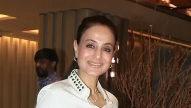 Ameesha Patel smiling at an event in Mumbai, wearing a white outfit with jewelry.
