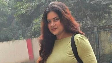 Portrait of a young woman with long dark hair wearing a green top and black backpack.