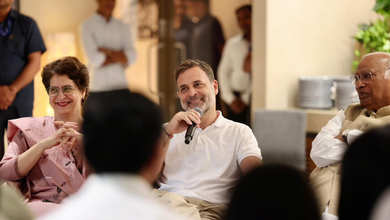 Rahul Gandhi speaking at a public event with smiling attendees around him.
