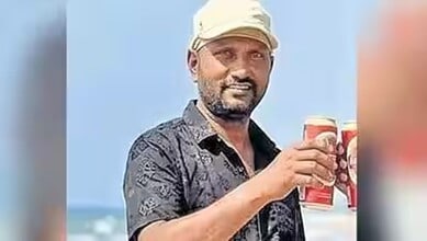 Man holding two cans of beverage outdoors with a blue sky background.