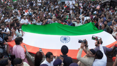 Large crowd holding a giant Indian flag during a protest rally in Delhi.
