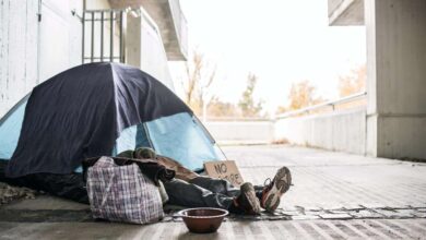 Legs and feet of homeless beggar man lying on the ground in city, sleeping in tent.