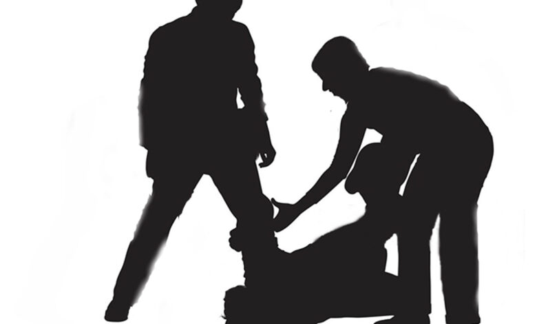 Two men assaulting another man who is lying on the ground.