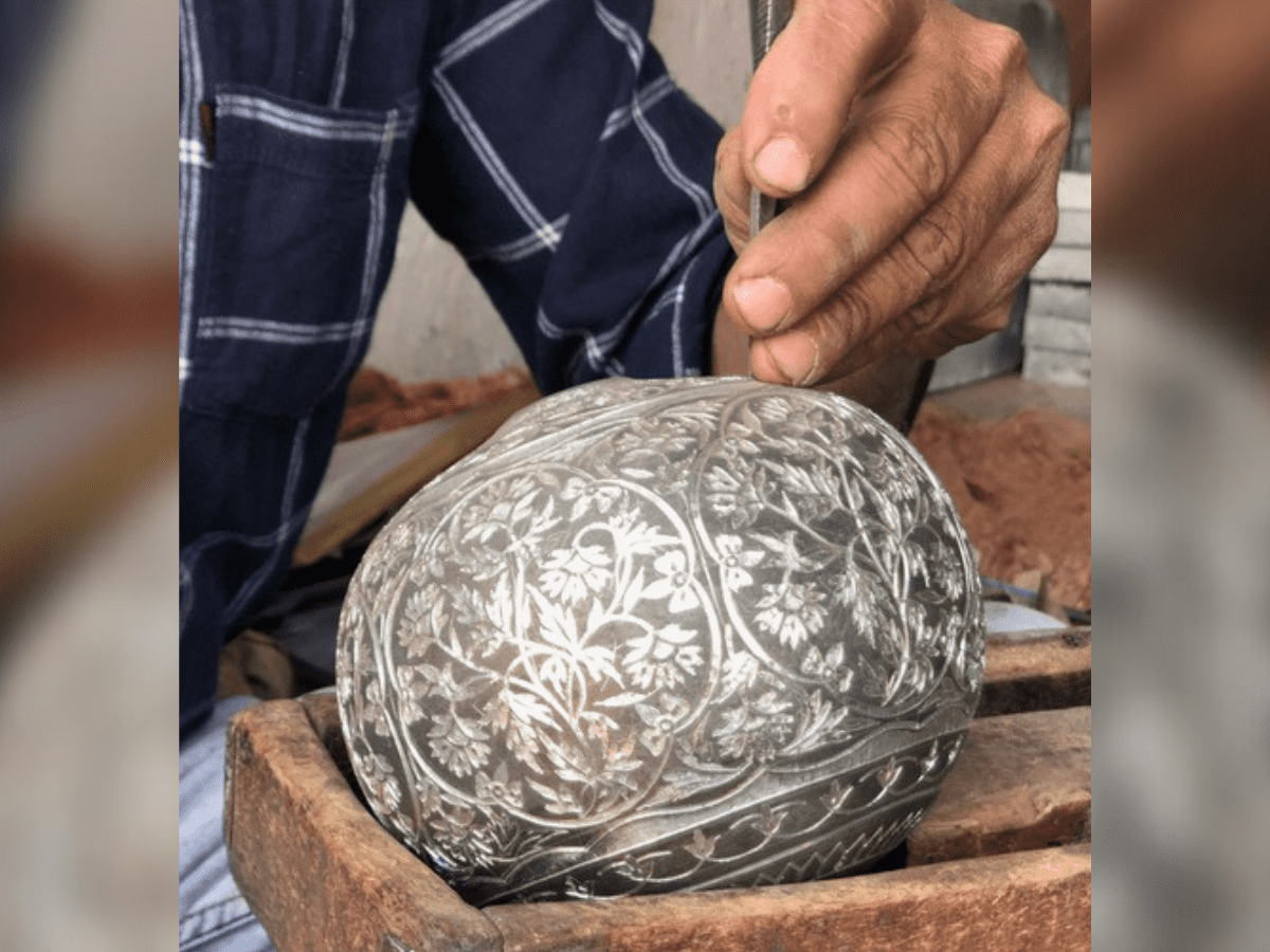 A Bidriware artisan carrying out silver inlay work on a hookah base.
