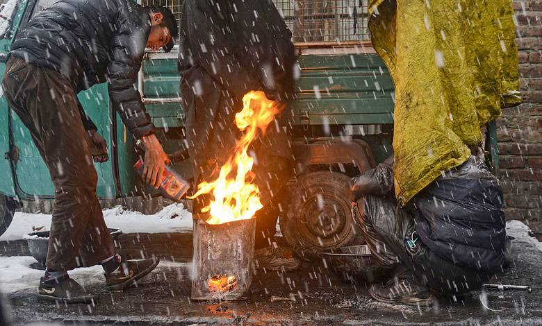 People warm themselves around a bonfire amid season's first snowfall, in Srinagar
