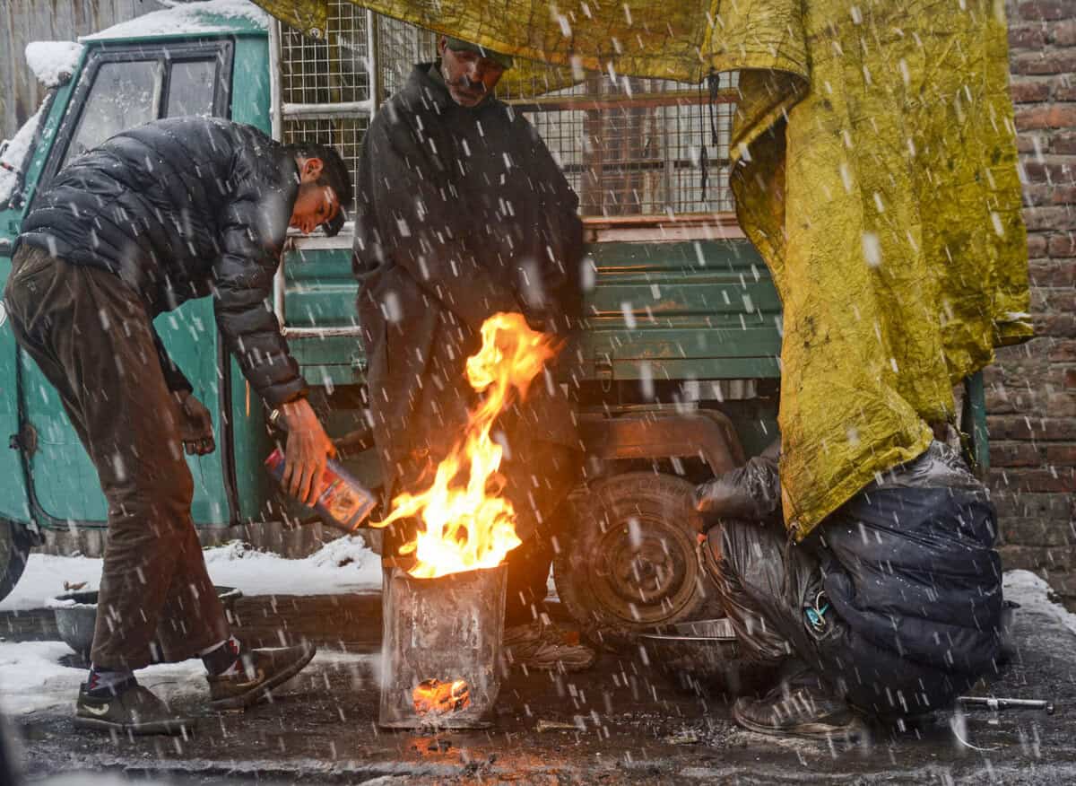 People warm themselves around a bonfire amid season's first snowfall, in Srinagar