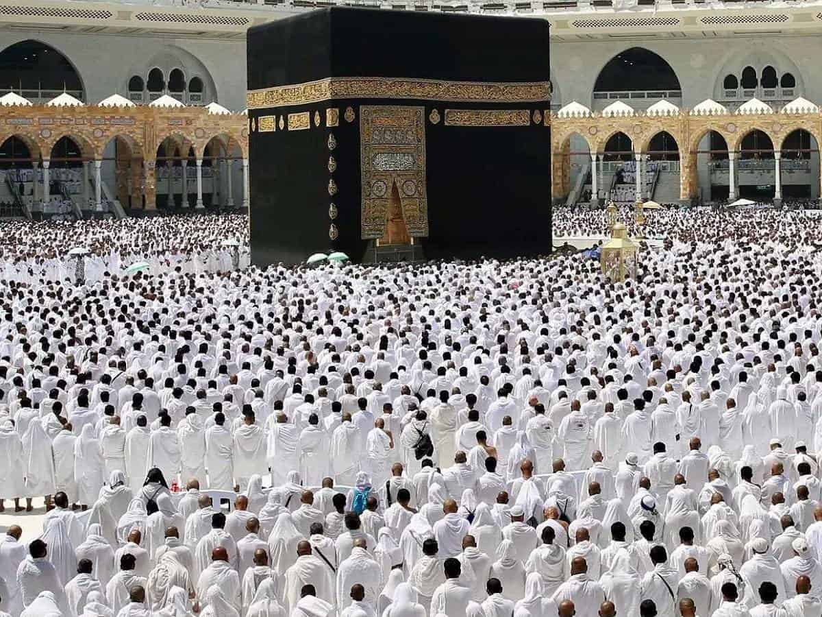 A vast congregation of Muslim worshippers, dressed in white ihram garments, gathers around the Kaaba at the Grand Mosque (Masjid al-Haram) in Makkah, Saudi Arabia, for the last Friday prayer of Ramzan. The sacred black-draped Kaaba stands at the centre, adorned with golden Arabic calligraphy.
