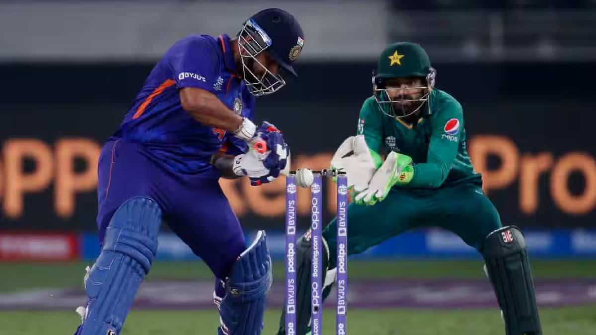 A couple of men playing cricket outdoors on a grassy field, wearing sports uniforms and using cricket bats and balls in a game setting.