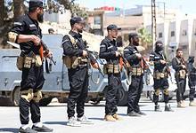 Syrian security forces in black uniforms standing in formation with rifles during a street deployment in a southern suburb of Damascus amid ongoing clashes.