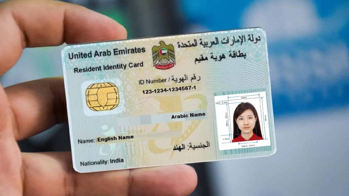Representative image shows a person holding a UAE Emirates ID card for a resident, featuring a smart chip, ID number, and a passport-sized photo of a woman. The ID displays English and Arabic text, including the name field and nationality marked as India. The background is blurred, highlighting the identification card in focus.