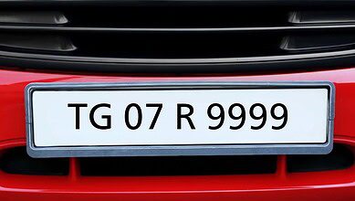 A red car's front bumper with a white license plate, gray border, showing "TG 07 R 9999" in black. "TG" is Telangana, "07" is RTO code, "R 9999" is the vehicle number. Black air vents are above and below the plate.