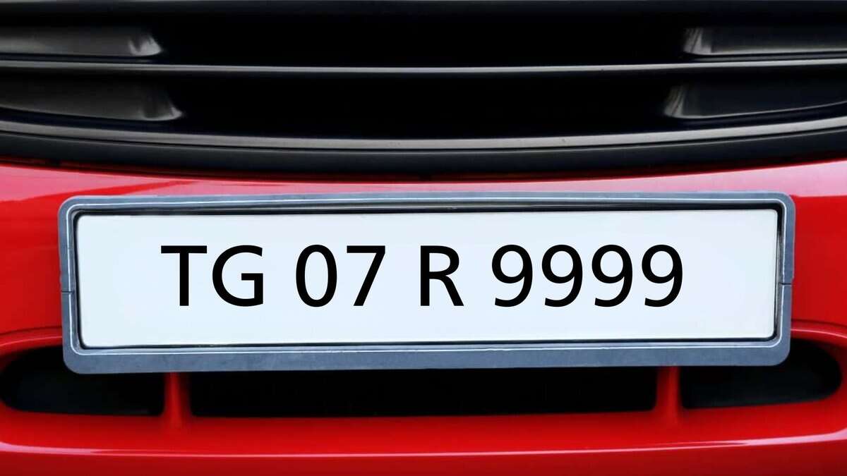 A red car's front bumper with a white license plate, gray border, showing