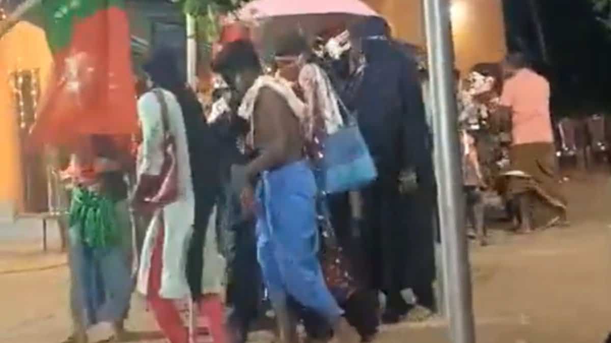 A group of men perform a dance dressed in various women's clothing, including one wearing a burqa, during a festival event in Karnataka.