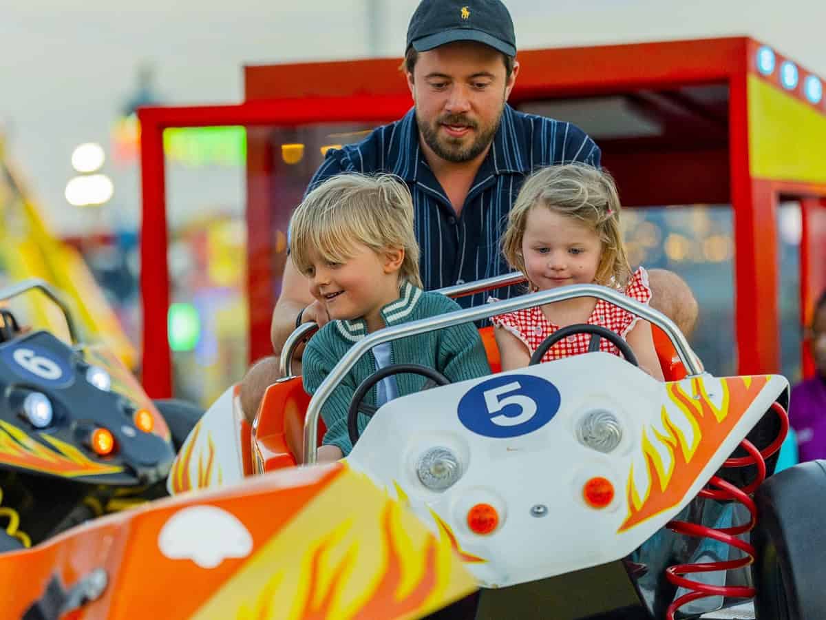 Father with two young children enjoying a car ride at Global Village Dubai funfair.