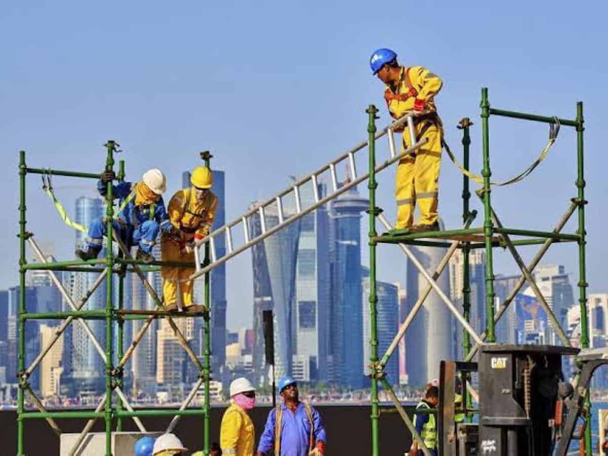 Construction workers on scaffolding at a building site in a Gulf city, wearing safety helmets and high-visibility clothing.