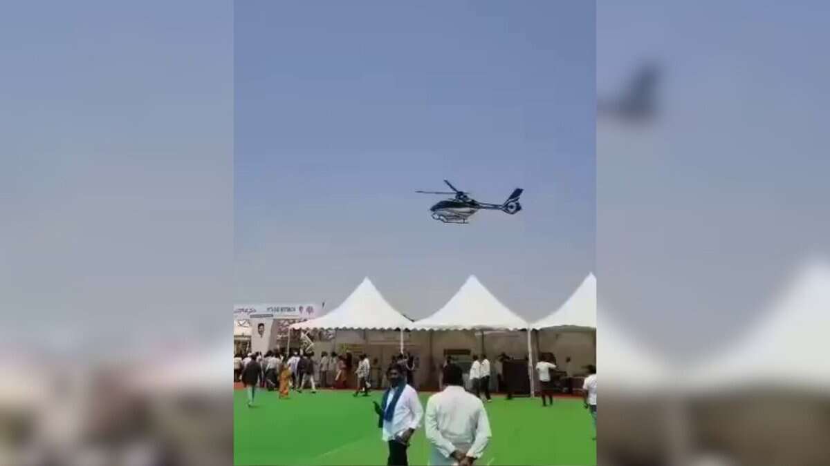 A helicopter hovers low over tents at the Rythu Mahotsav event in Nizamabad, as people look on and begin to move away.