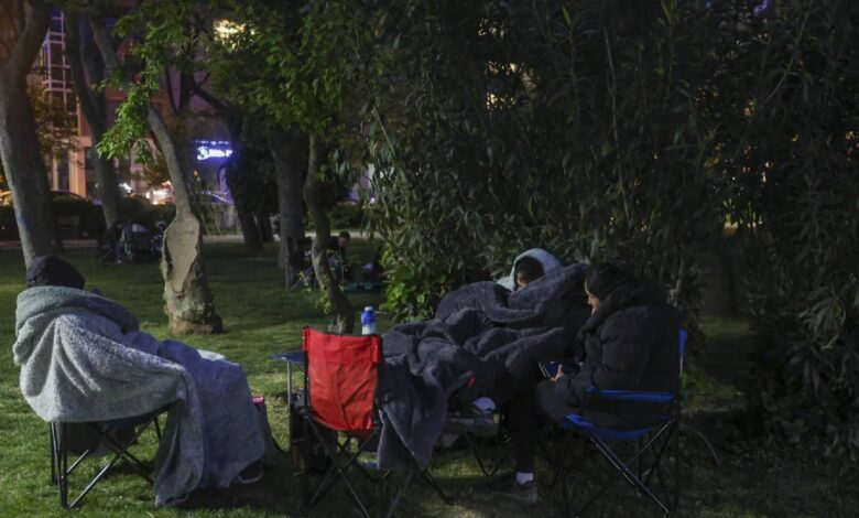 Istanbul residents wrapped in blankets and sitting on camping chairs in a park at night, seeking safety outdoors after a 6.2 magnitude earthquake and ongoing aftershocks.