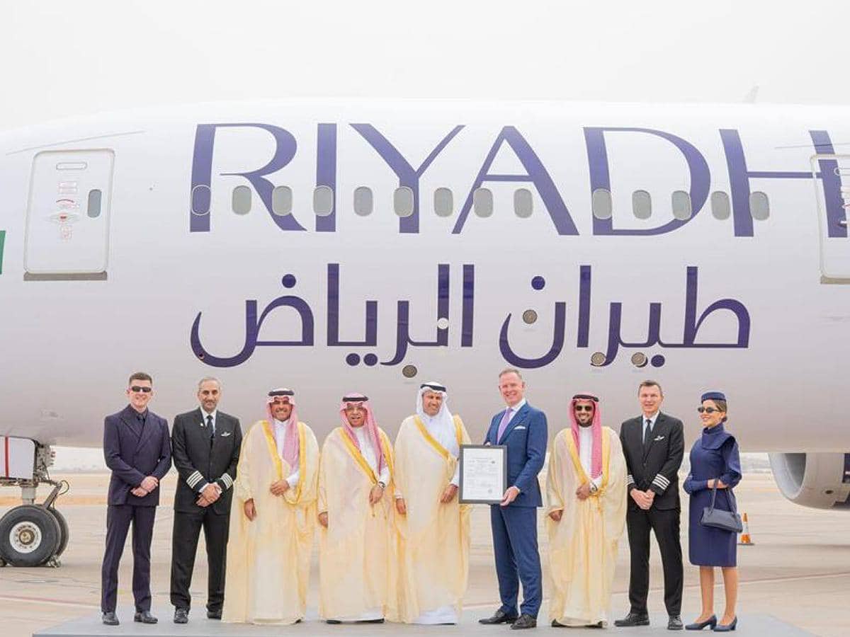 A group of dignitaries, executives, and crew members pose in front of a Riyadh Air airplane.