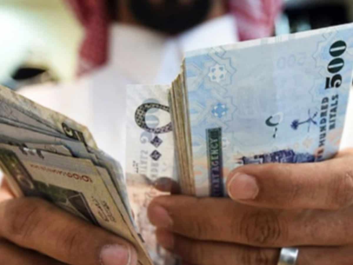 Representative image shows man counting Saudi riyal banknotes.