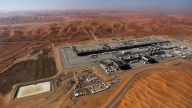 Aerial view of oil or gas processing facility in the Saudi Arabian desert, surrounded by sand dunes under clear skies.