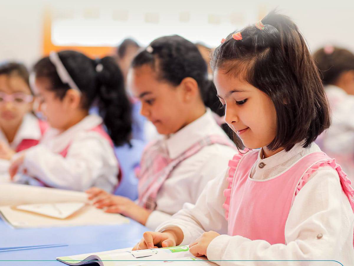 Young Saudi girls in a classroom wearing pink uniforms, engaged in learning activities at a Saudi school.