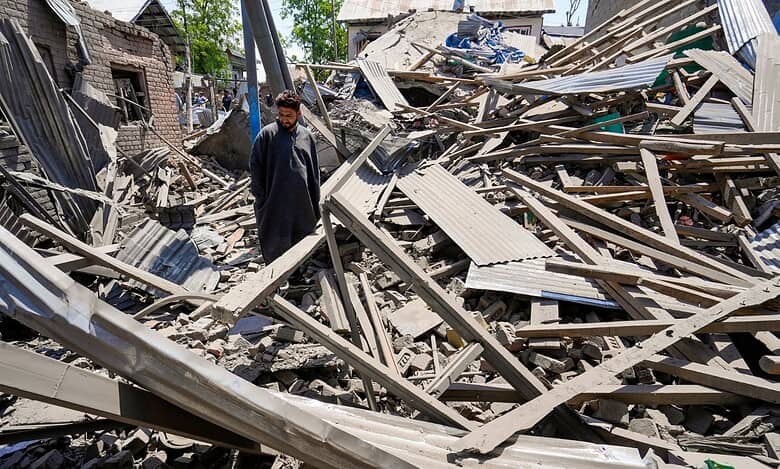 The image displays a man standing between the remains of a demolished house in Kashmir. April 26, 2025