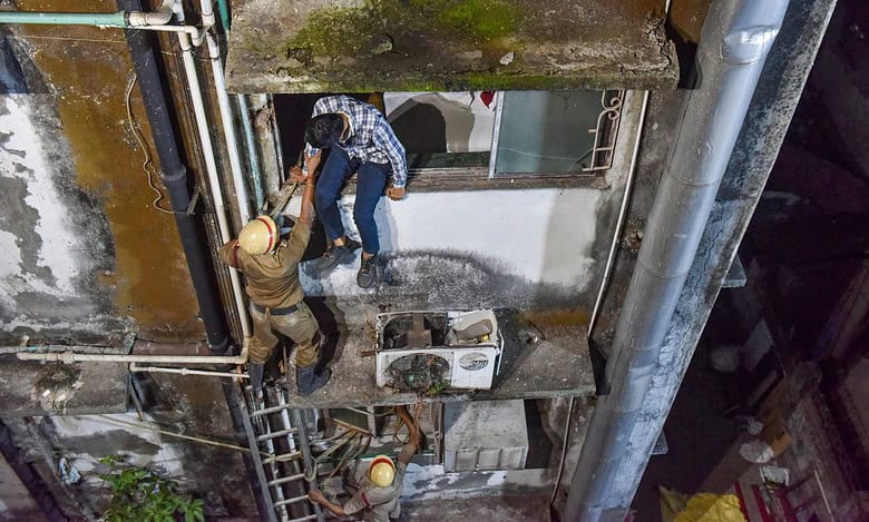 The image displays a picture of firefighters evacuating people after a fire broke out at a hotel in Kolkata on late Tuesday night.
