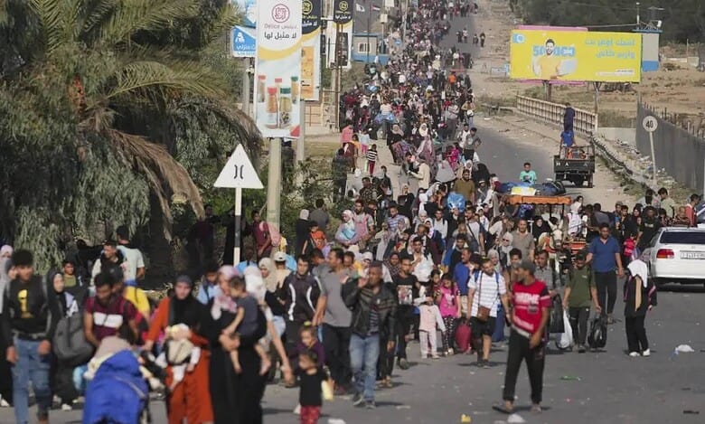 Displaced Palestinian families flee on foot along a road in Gaza, carrying belongings amid Israeli military strikes and displacement orders.