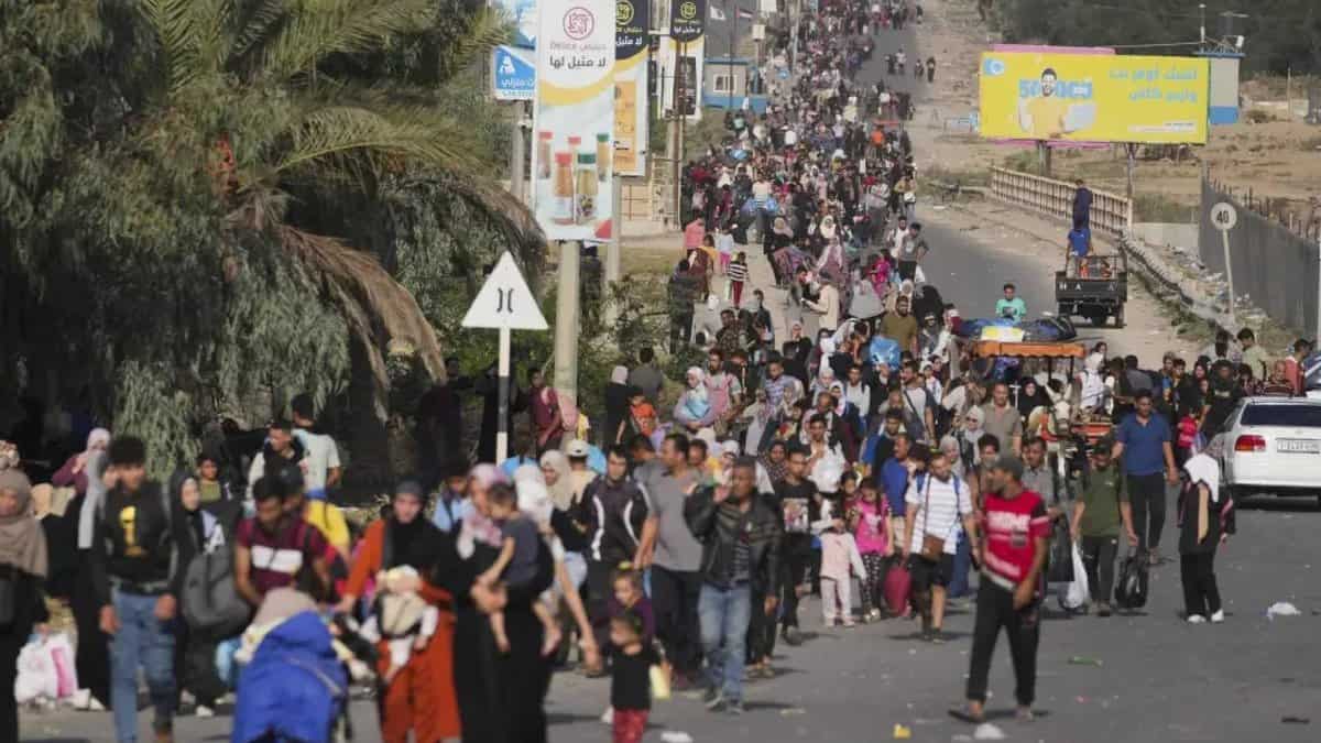 Displaced Palestinian families flee on foot along a road in Gaza, carrying belongings amid Israeli military strikes and displacement orders.