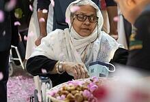 Elderly female Haj pilgrim in wheelchair welcomed with rose petals and traditional dates on arrival in Saudi Arabia for Haj 2025.