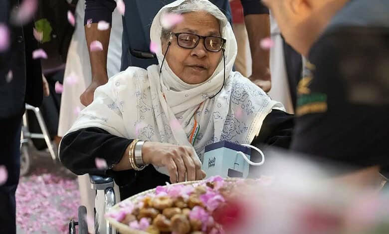 Elderly female Haj pilgrim in wheelchair welcomed with rose petals and traditional dates on arrival in Saudi Arabia for Haj 2025.