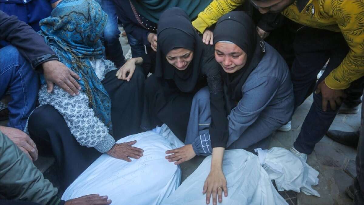Grieving Palestinian women mourn beside bodies wrapped in shrouds after Israeli strikes in Gaza.