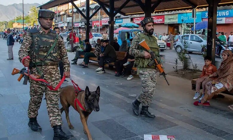 Indian troops patrol a busy market street in Srinagar, Jammu and Kashmir, with sniffer dogs and rifles, as civilians observe, amid heightened security following recent attacks.