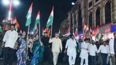 A large group marches at night holding Indian flags, including leaders and civilians, celebrating national unity and pride.