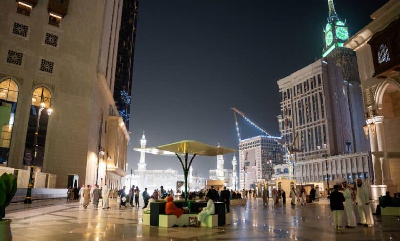 Night view of pilgrims using the new walkway from Address Jabal Omar Makkah to the Grand Mosque, with the iconic clock tower illuminated in the background.