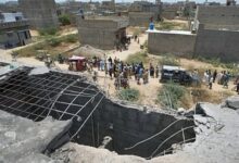 A large hole is visible on the rooftop of a structure reportedly damaged in a suspected Indian drone strike, as residents gather near a cordoned-off area where Pakistan's air defence system shot down the drone in Karachi on May 8.