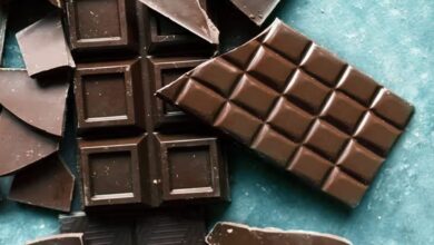 Broken dark chocolate bars scattered on a teal surface, some pieces in squares, others in irregular chunks, showcasing a rich, glossy texture.