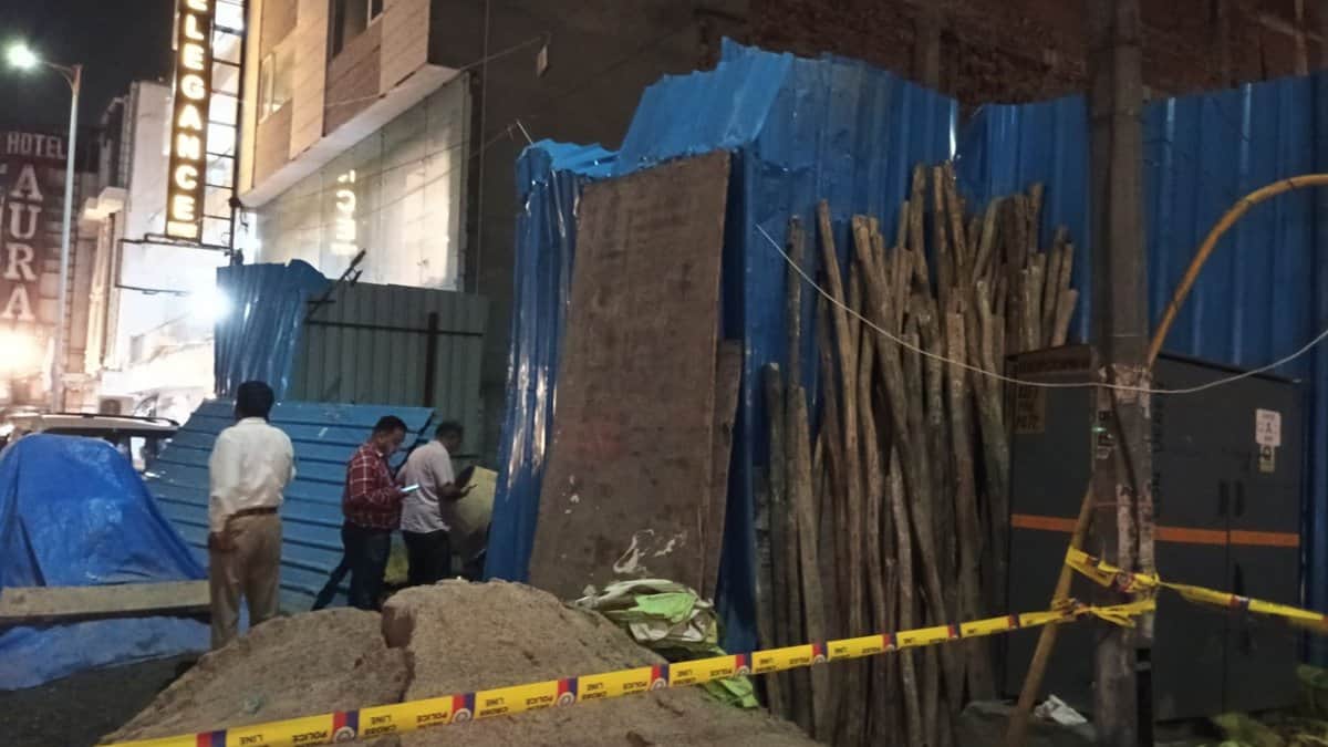 At night, police tape cordons off a collapsed building site near Hotel Elegance, with debris, sand, and workers inspecting the scene under streetlights.