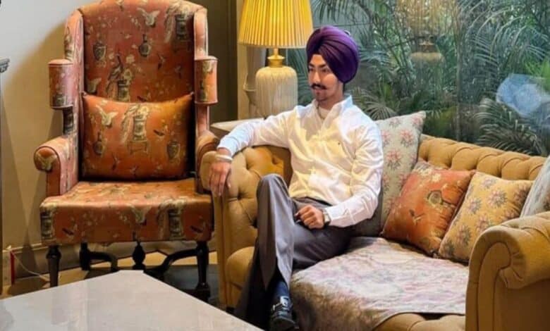 A well-dressed Sikh man wearing a purple turban sits confidently on a sofa in a stylish, well-lit living room with classic decor.