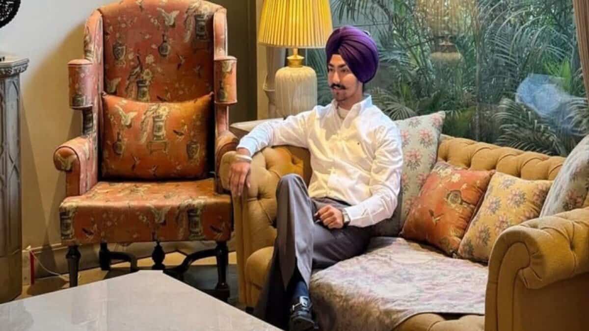 A well-dressed Sikh man wearing a purple turban sits confidently on a sofa in a stylish, well-lit living room with classic decor.