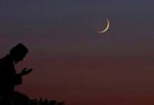 A silhouette of a person praying under a twilight sky with a crescent moon visible above.