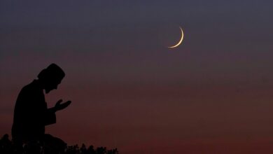 A silhouette of a person praying under a twilight sky with a crescent moon visible above.
