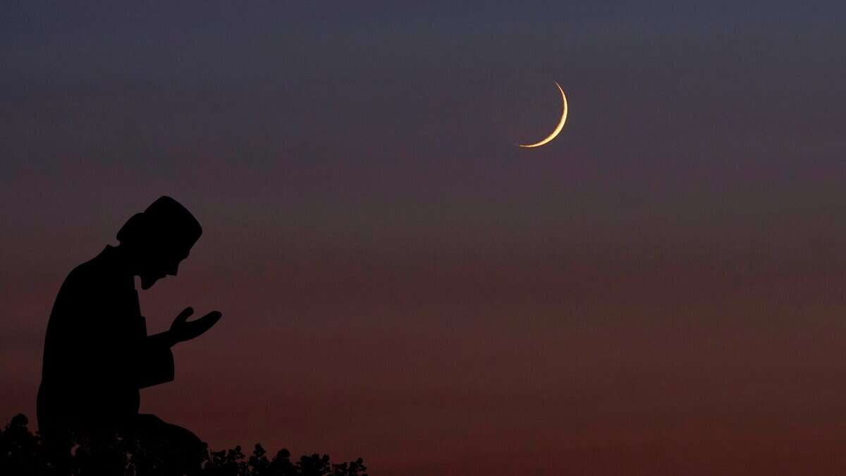 A silhouette of a person praying under a twilight sky with a crescent moon visible above.