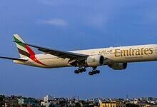 Emirates Boeing 777 aircraft flying low over a cityscape during landing, with landing gear deployed.