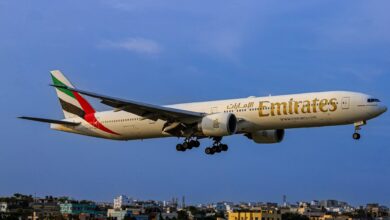 Emirates Boeing 777 aircraft flying low over a cityscape during landing, with landing gear deployed.