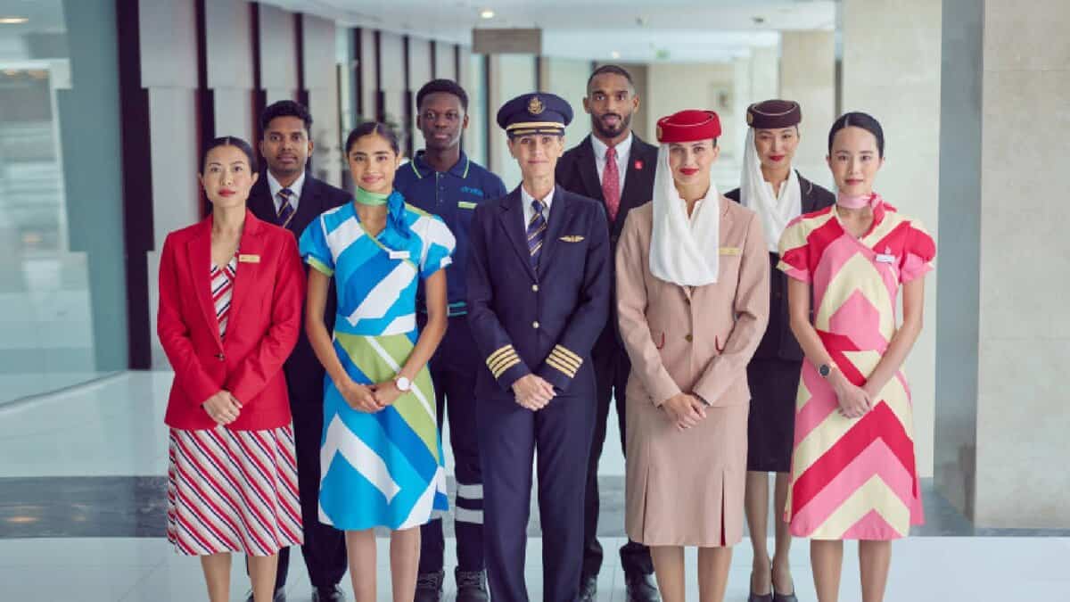 A diverse group of Emirates Group staff, including pilots, cabin crew, and ground personnel, standing in uniform at a modern airport terminal. The image showcases multicultural representation and professional airline attire.