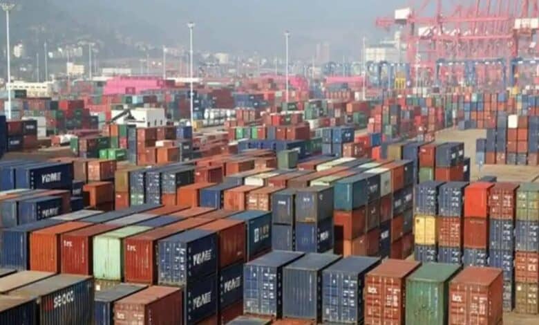 Hundreds of colorful shipping containers stacked at a busy port terminal with cranes and a hazy cityscape in the background