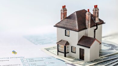 A model of a house placed on US dollar bills, with property-related documents underneath, symbolising property ownership, real estate investment, or property tax payments for GHMC property tax collection story.