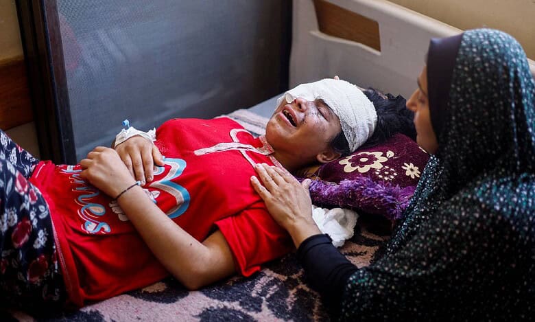 Injured Palestinian girl with bandaged eyes lies on a hospital bed in Gaza, comforted by a woman, during Israel’s ongoing assault on the Gaza Strip.