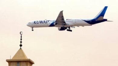 Kuwait Airways aircraft flying over mosque minaret with crescent moon symbol, approaching landing during daylight.
